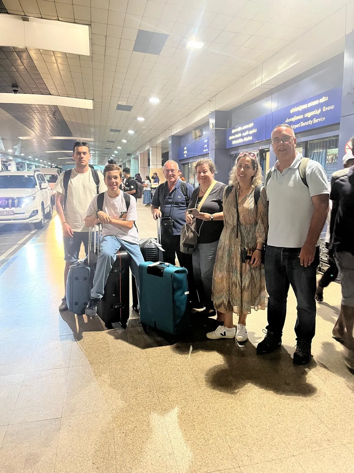 A group of travellers with their luggage meeting their driver in the airport arrivals hall